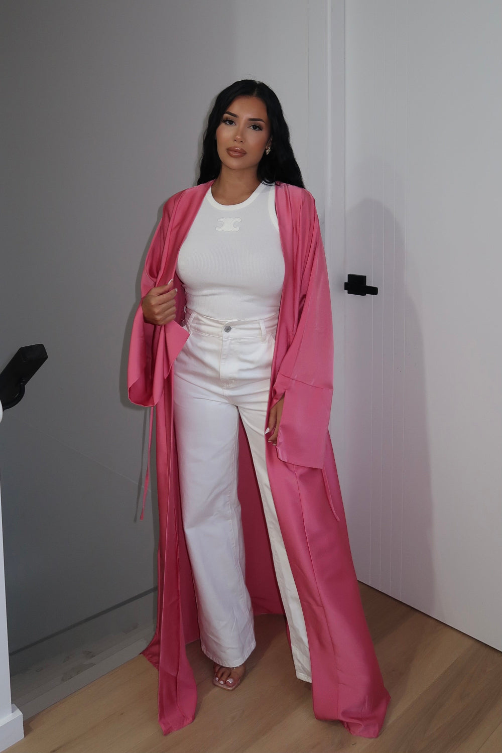 Woman wearing a pink coat over a white outfit in a minimal indoor setting